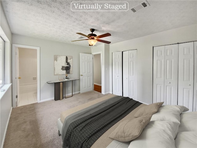 carpeted bedroom with ceiling fan, a textured ceiling, connected bathroom, and multiple closets