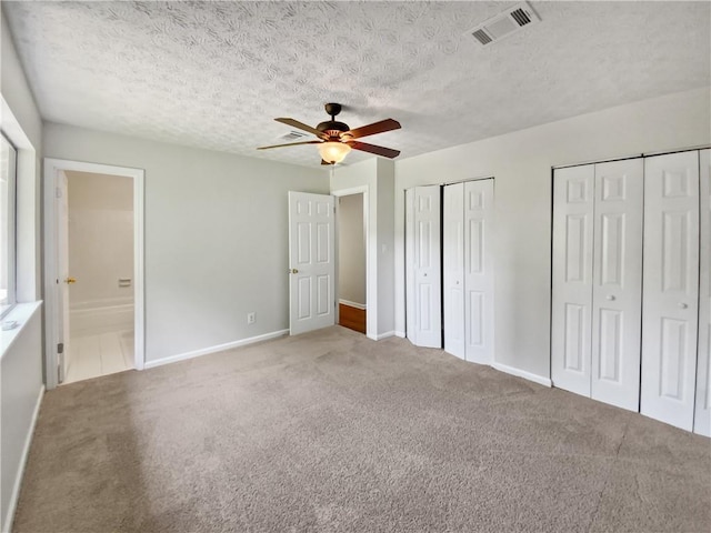 unfurnished bedroom featuring two closets, ceiling fan, a textured ceiling, connected bathroom, and carpet floors