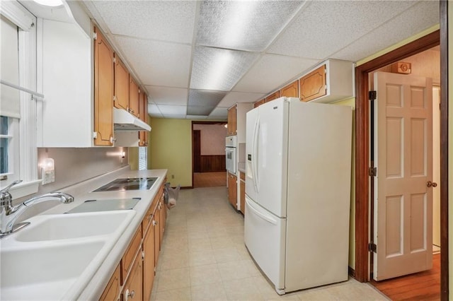 kitchen featuring light countertops, a sink, white appliances, a drop ceiling, and under cabinet range hood