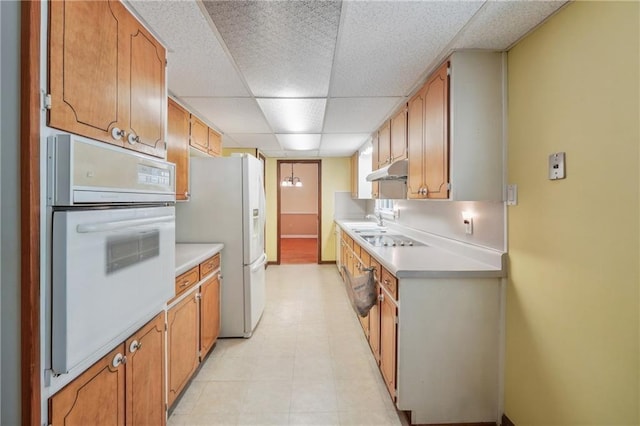 kitchen with a paneled ceiling, light countertops, a sink, white appliances, and under cabinet range hood