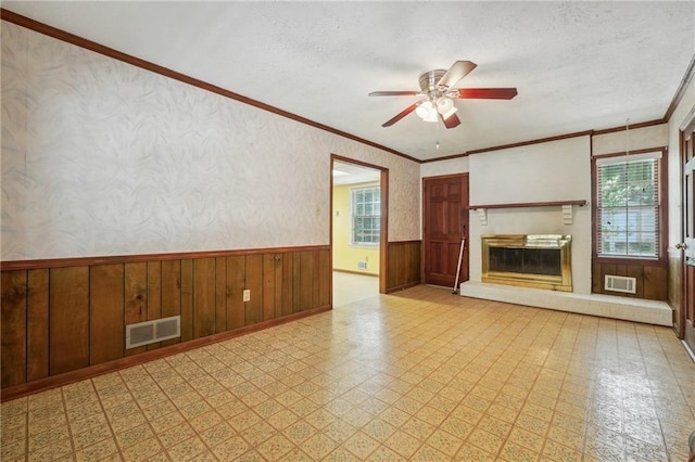 unfurnished living room with a wainscoted wall, visible vents, a glass covered fireplace, and tile patterned floors