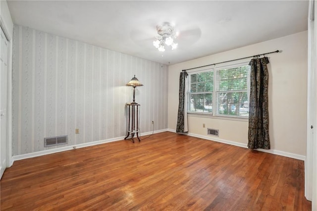 empty room with a ceiling fan, baseboards, visible vents, and wood finished floors