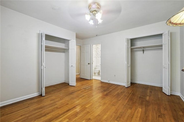 unfurnished bedroom with baseboards, ensuite bathroom, multiple closets, and wood finished floors