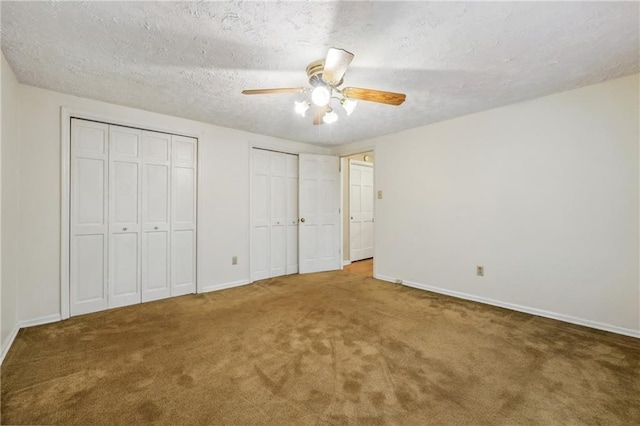 unfurnished bedroom with carpet, a textured ceiling, baseboards, and two closets