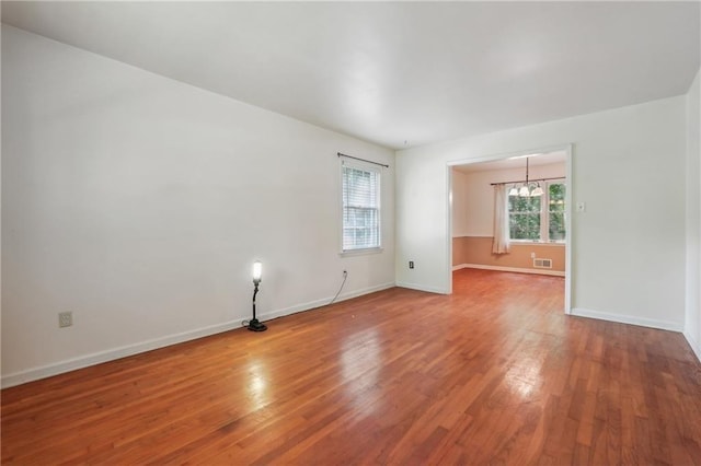 spare room featuring an inviting chandelier, wood finished floors, visible vents, and baseboards