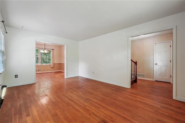 unfurnished room featuring baseboards, visible vents, wood finished floors, stairs, and a chandelier