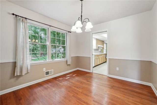 empty room with baseboards, a notable chandelier, visible vents, and light wood-style floors