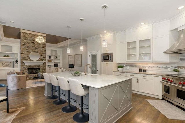 kitchen with light stone countertops, stainless steel appliances, a fireplace, white cabinets, and a center island with sink