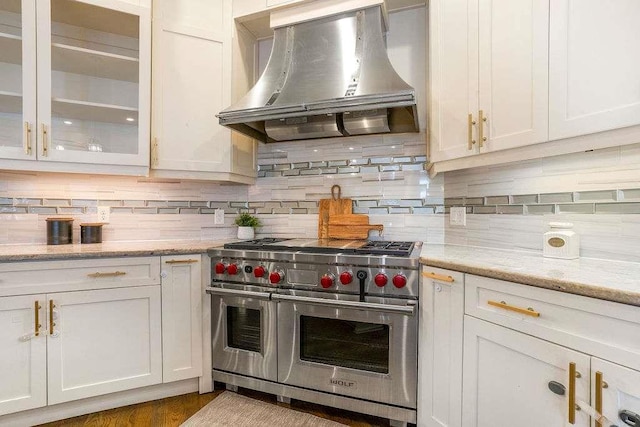 kitchen with white cabinetry, tasteful backsplash, light stone counters, double oven range, and exhaust hood