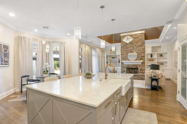 kitchen featuring built in shelves, decorative light fixtures, a kitchen island with sink, and hardwood / wood-style floors