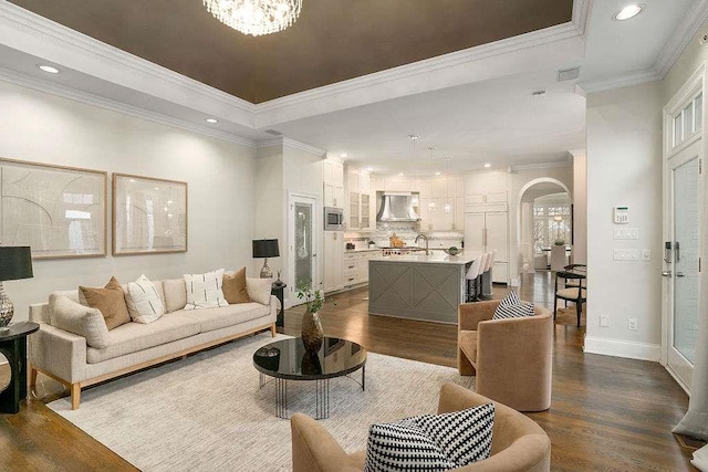 living room with sink, an inviting chandelier, a raised ceiling, dark hardwood / wood-style flooring, and crown molding