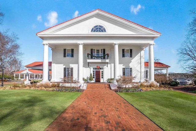 greek revival inspired property featuring a balcony and a front yard