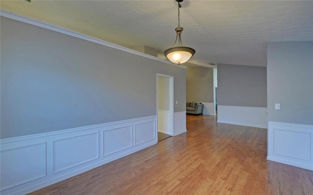 unfurnished room featuring light wood-style floors, a decorative wall, and a wainscoted wall