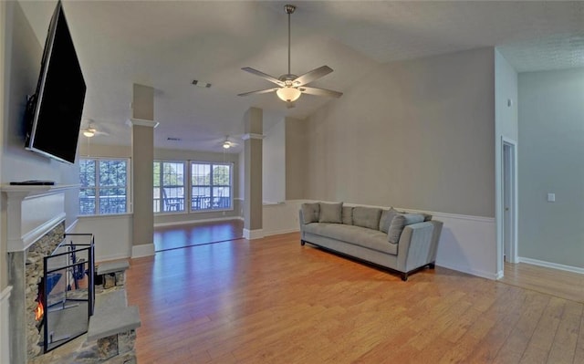 living room featuring a stone fireplace, light wood-style floors, ceiling fan, lofted ceiling, and visible vents
