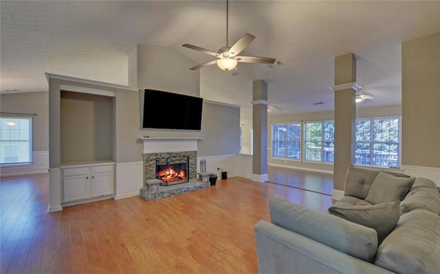 living area featuring lofted ceiling, light wood finished floors, decorative columns, a fireplace, and ceiling fan