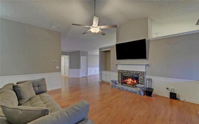 living room with ceiling fan, a stone fireplace, lofted ceiling, and wood finished floors