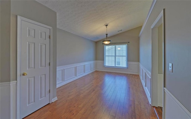 unfurnished dining area featuring vaulted ceiling, a wainscoted wall, hardwood / wood-style floors, and a textured ceiling