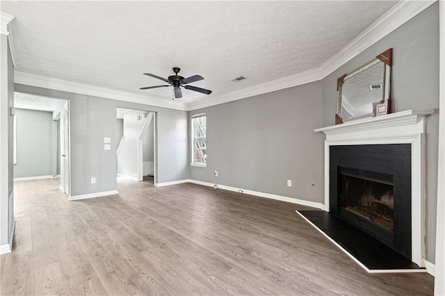 unfurnished living room featuring crown molding, a fireplace with raised hearth, visible vents, a ceiling fan, and wood finished floors