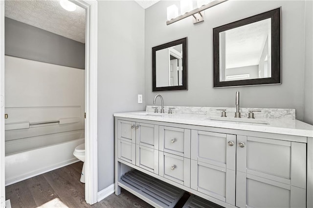 bathroom with double vanity, a textured ceiling, a sink, and wood finished floors