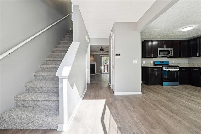 staircase with a fireplace, ceiling fan, a textured ceiling, wood finished floors, and baseboards