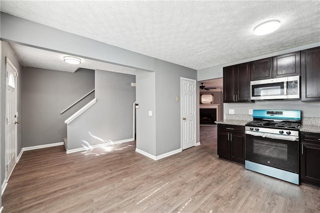 kitchen with baseboards, stainless steel appliances, a textured ceiling, light wood-type flooring, and a fireplace