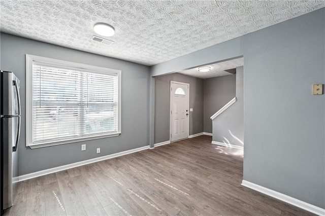 foyer entrance featuring a textured ceiling, wood finished floors, visible vents, and baseboards