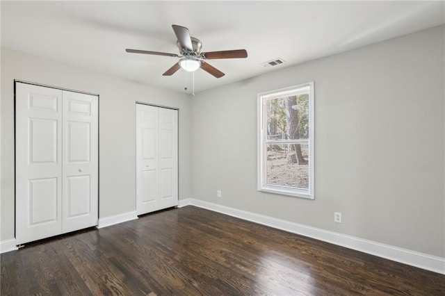 unfurnished bedroom featuring ceiling fan, dark hardwood / wood-style floors, and multiple closets