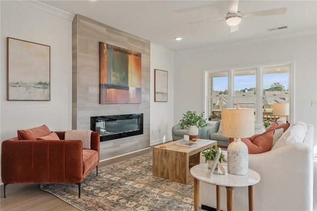 living room featuring visible vents, ornamental molding, a ceiling fan, wood finished floors, and a tile fireplace