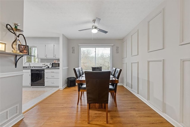 dining space featuring sink, light hardwood / wood-style floors, a textured ceiling, and ceiling fan