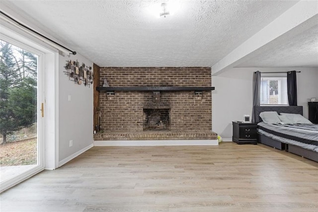 bedroom featuring access to exterior, a textured ceiling, light hardwood / wood-style flooring, and a brick fireplace