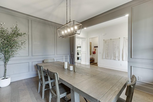 dining space featuring an inviting chandelier, a decorative wall, and wood finished floors