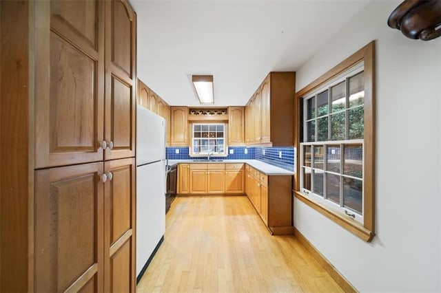 kitchen featuring white refrigerator, sink, light hardwood / wood-style flooring, and backsplash