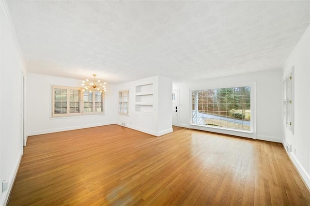 unfurnished living room with an inviting chandelier, built in shelves, wood-type flooring, and a textured ceiling