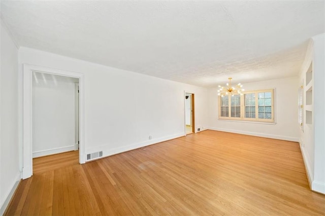 spare room with a chandelier and light wood-type flooring