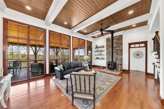 living room with beamed ceiling, ceiling fan, a wood stove, and wood-type flooring