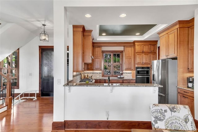 kitchen featuring dark stone counters, tasteful backsplash, stainless steel appliances, a raised ceiling, and dark hardwood / wood-style flooring