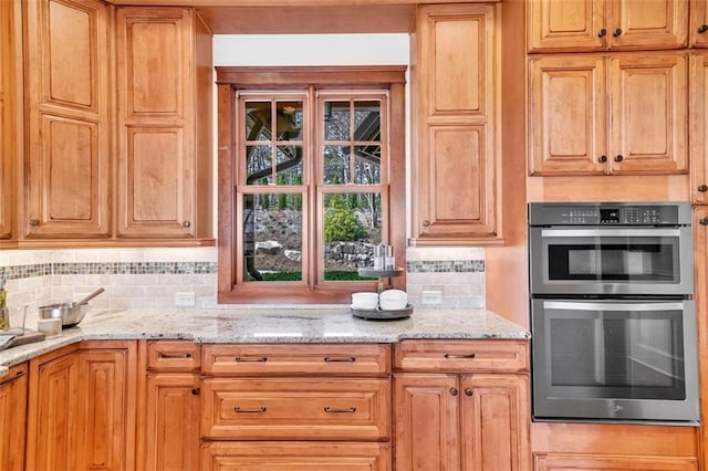 kitchen featuring light stone counters, stainless steel double oven, and tasteful backsplash