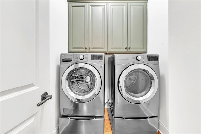 clothes washing area with washing machine and clothes dryer, hardwood / wood-style flooring, and cabinets