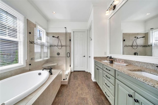 bathroom with double sink, vanity with extensive cabinet space, shower with separate bathtub, ornamental molding, and hardwood / wood-style flooring