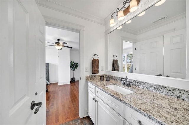 bathroom featuring crown molding, ceiling fan, vanity with extensive cabinet space, and hardwood / wood-style floors