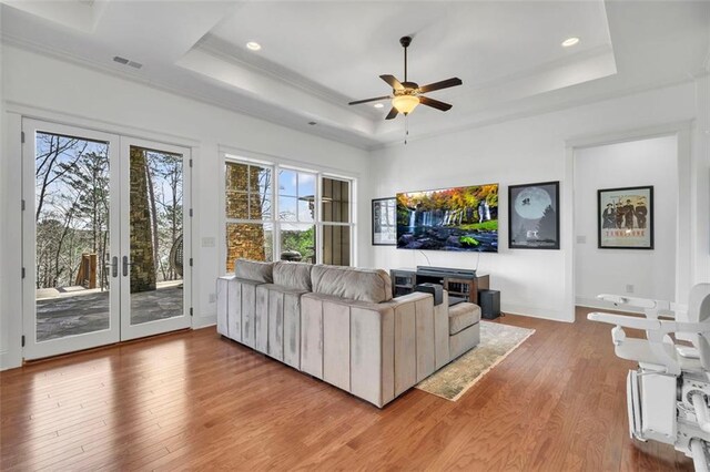 living room featuring wood-type flooring, ceiling fan, and a raised ceiling