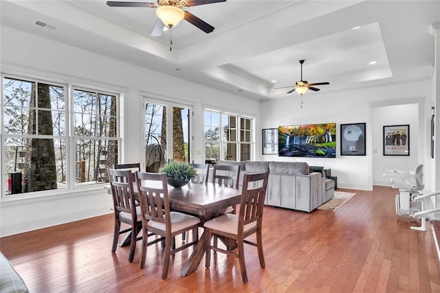 dining space with ceiling fan, a tray ceiling, and wood-type flooring