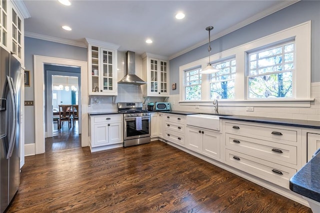 kitchen with wall chimney range hood, sink, hanging light fixtures, stainless steel appliances, and white cabinets