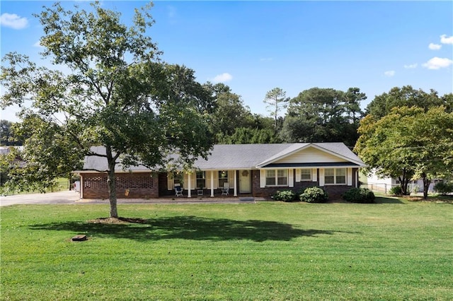 single story home featuring driveway, brick siding, covered porch, and a front yard