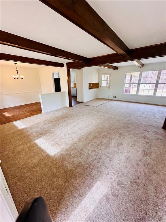 unfurnished living room with beam ceiling, a notable chandelier, carpet, and baseboards