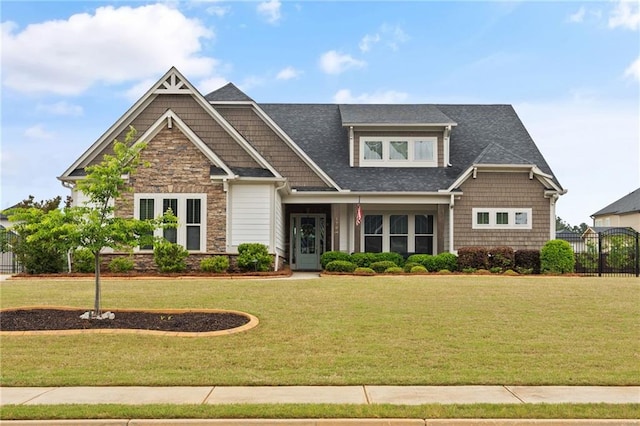 craftsman inspired home featuring a shingled roof, a front lawn, fence, and stone siding