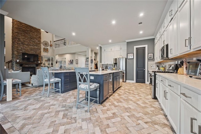 kitchen with a kitchen island, a kitchen bar, appliances with stainless steel finishes, white cabinets, and open floor plan