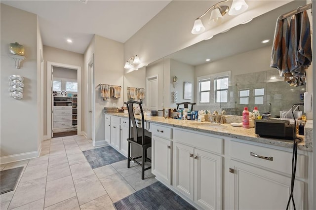 bathroom with vanity, baseboards, a walk in closet, and a tile shower