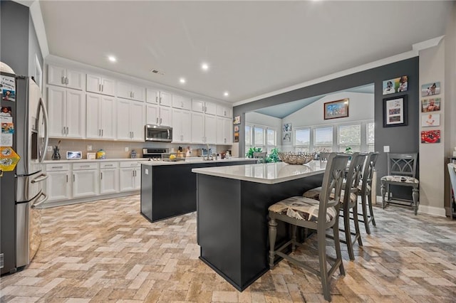 kitchen with a center island, light countertops, white cabinets, a breakfast bar, and stainless steel appliances
