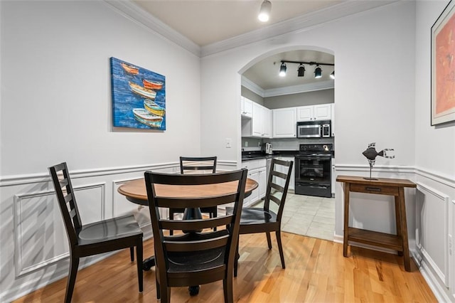 dining room featuring track lighting, crown molding, arched walkways, light wood-type flooring, and wainscoting